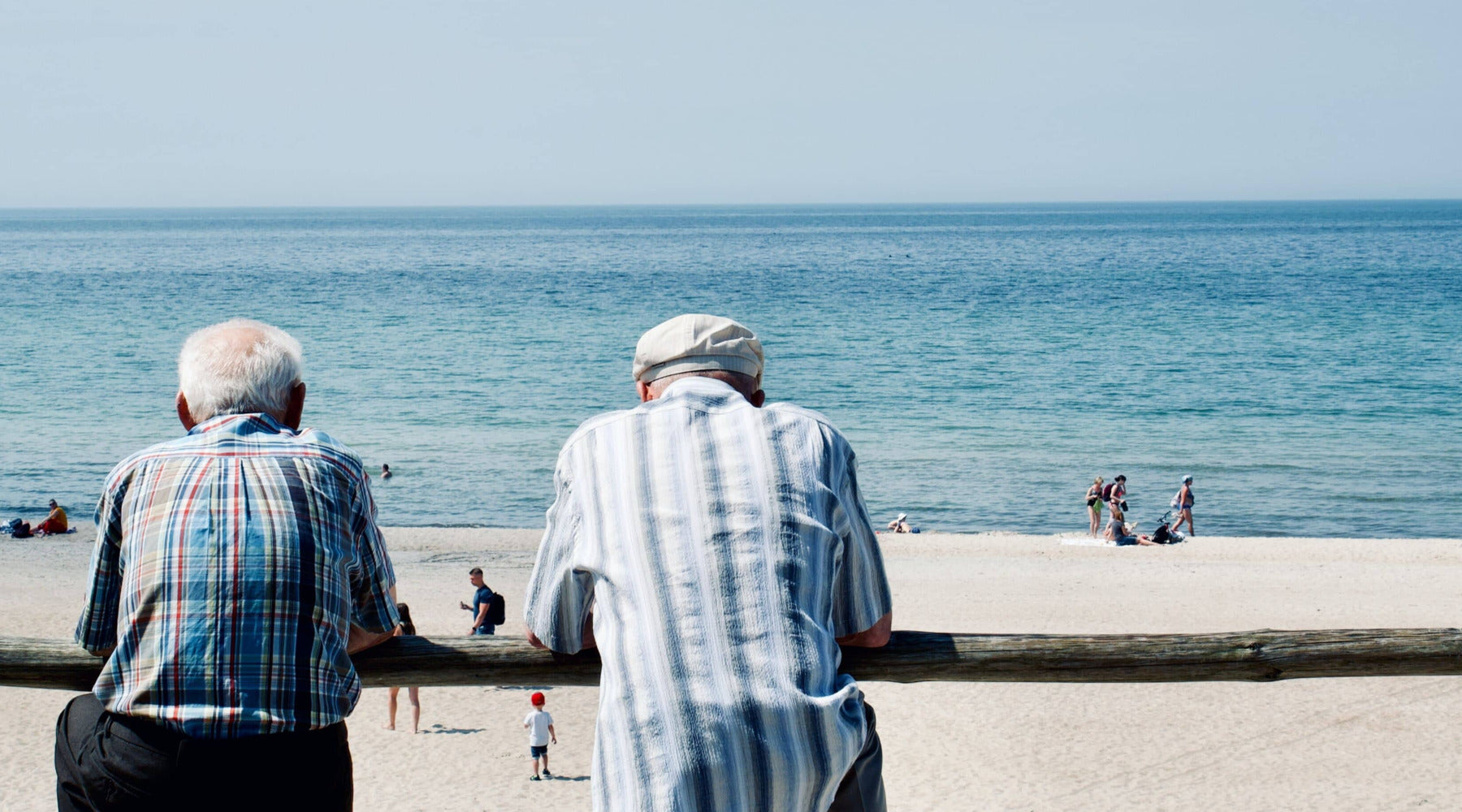 two old men, leaning on a wodden fence. Looking out at the beach and a crystal blue ocean.